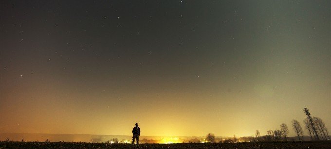 Ensam man står på en åker och tittar upp i himlen.