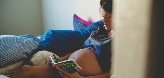 Gravid kvinna läser barnbok i säng.