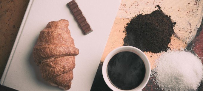 En croissant, en bit choklad och en kopp kaffe på ett bord.