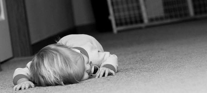 En bebis ligger på mage på golvet.