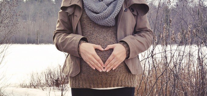 Gravid som står ute på landet och håller om sin gravida mage.
