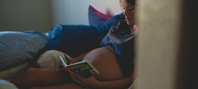 En gravid kvinna läser en bok i sängen.