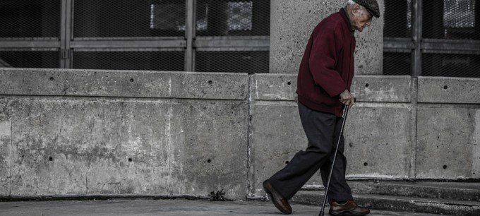 En äldre man går med en käpp.
