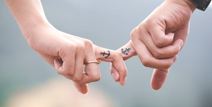 Fingrar som krokar ihop där båda pekfingrarna har tatuerat in ett ankare.