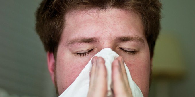 Man har fått ett virus i kroppen och snyter sig därför om näsan på grund av förkylning.