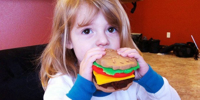 Liten tjej som äter en konstgjord hamburgare.